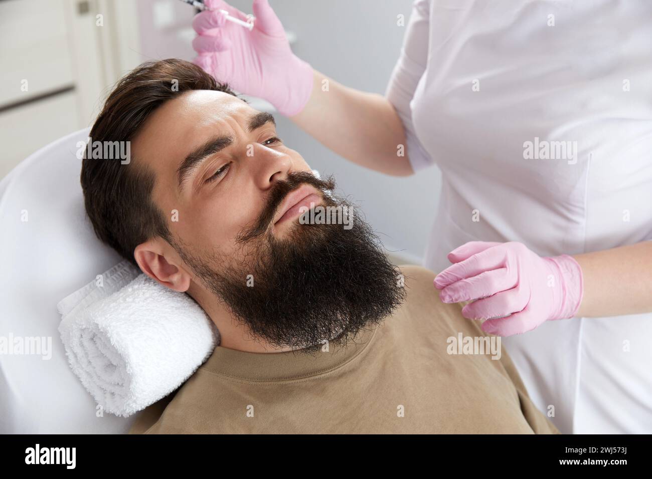 Primo piano di un uomo barbuto che riceve un'iniezione di bellezza alla clinica estetica. Chirurgo plastico iniettando il riempitivo anti-invecchiamento in un uomo bello Foto Stock