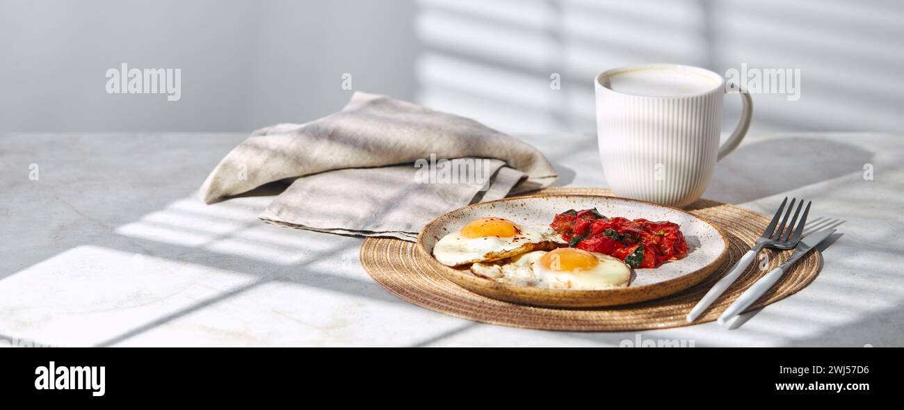 Colazione con uova fritte e pomodori fritti con spinaci sul piatto e tazza di caffè latte Foto Stock
