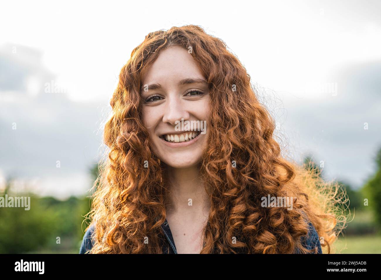 Donna rossa con capelli ricci sorridenti in luce naturale all'aperto - Un ritratto che cattura la gioia dei giovani e la bellezza naturale. Foto Stock