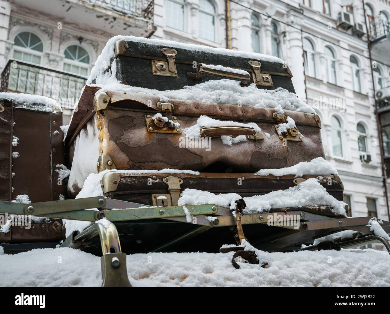 Valigie d'epoca coperte di neve sul tetto di un'auto sullo sfondo di una vecchia casa come concetto di viaggio. Foto Stock
