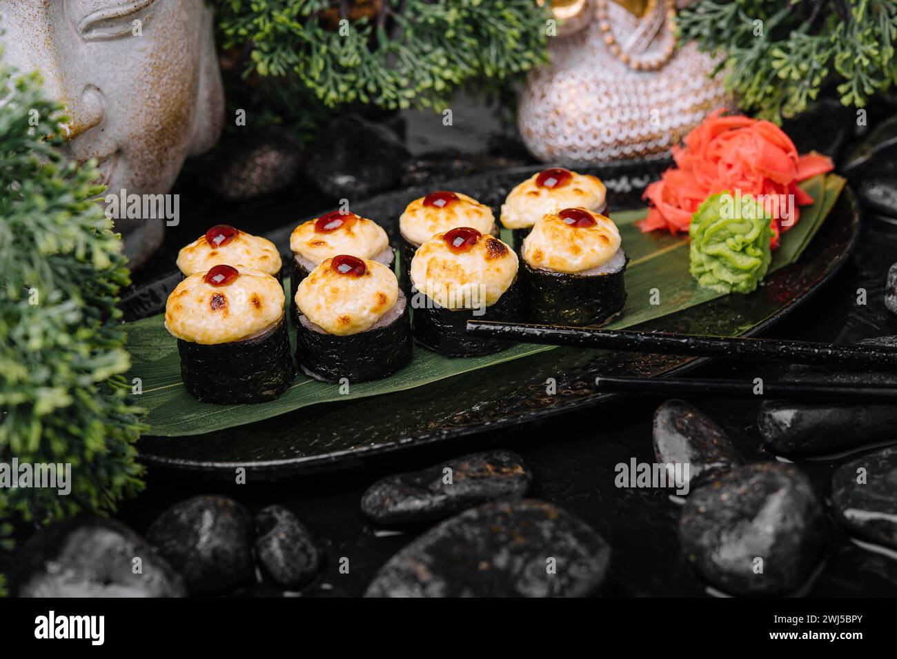 Servito sushi caldo arrotolato in lenzuola nori con zenzero e wasabi su un piatto di pietra nera Foto Stock