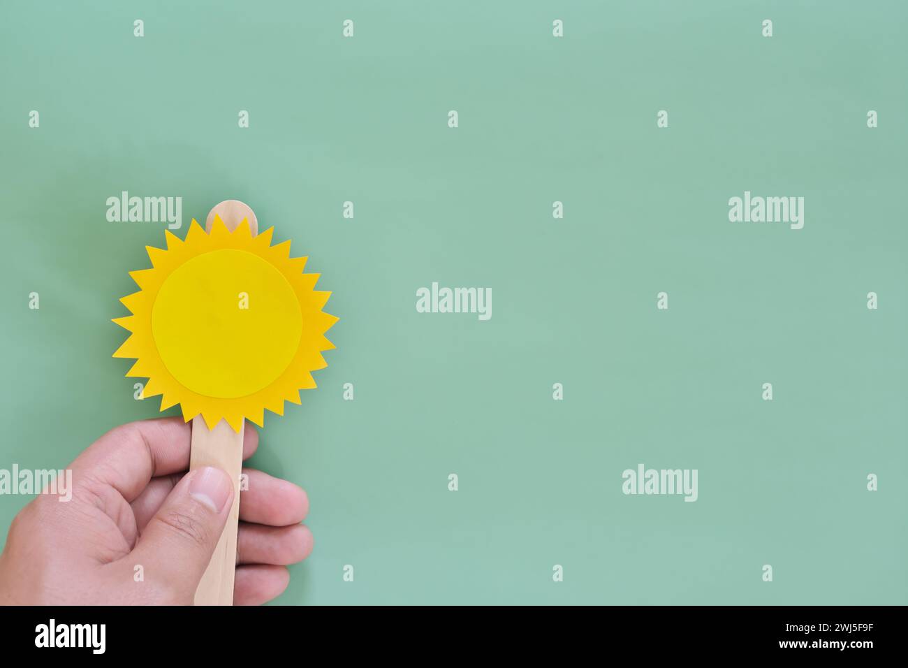 Mano umana che tiene la carta a forma di popsicle solare su sfondo verde con spazio di copia. Sfondo della stagione estiva. Foto Stock