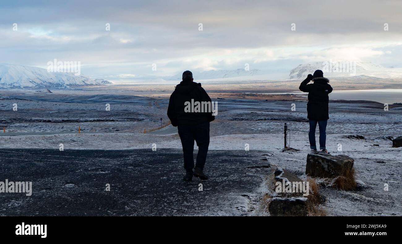 Vista posteriore di turisti anonimi in abiti caldi che si stagliano su un paesaggio innevato guardando il lago e le montagne ghiacciate durante le visite turistiche serali d'inverno Foto Stock