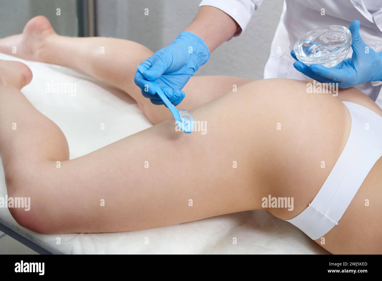 Il cosmetologo applica un gel trasparente alle gambe e alla natica del paziente per il trattamento di bellezza Foto Stock