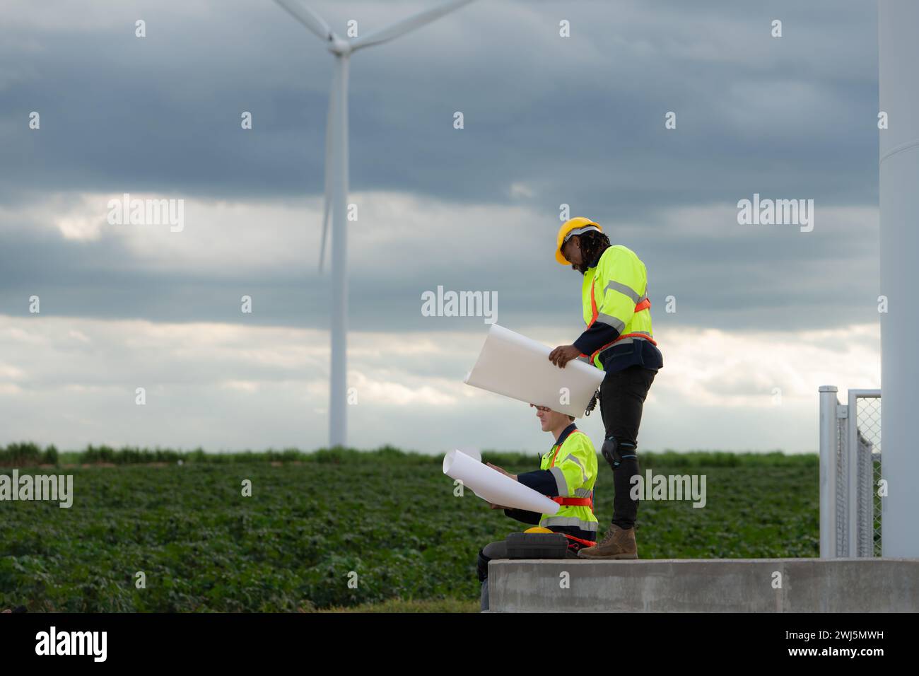 Ingegneri e tecnici lavorano insieme sulla base della torre di una grande turbina eolica con un campo di turbine eoliche sullo sfondo, T Foto Stock Ingegneri e tecnici lavorano insieme sulla base della torre di una grande turbina eolica con un campo di turbine eoliche sullo sfondo, T Foto Stock