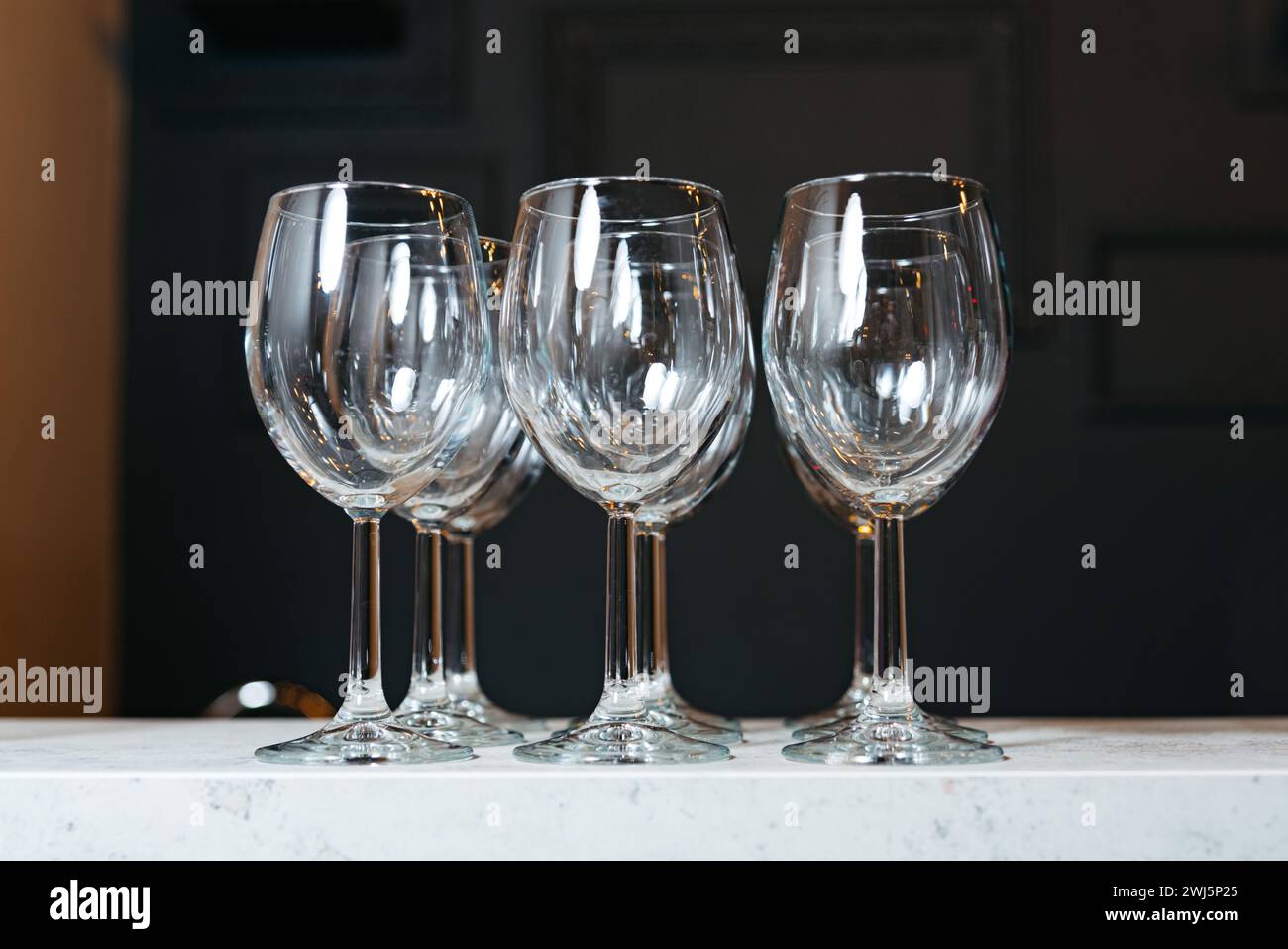 Un set di quattro bicchieri da vino in cristallo vuoti esposti su un piano di lavoro in marmo bianco che riflette la luce in modo splendido. Foto Stock