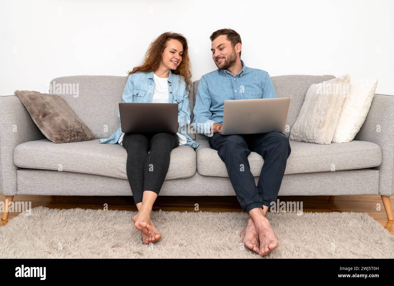 Donna e uomo si siedono sul divano usando il computer portatile e sorridono. Shopping online. Foto Stock