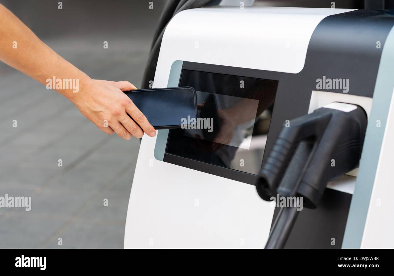 Tecnologia di pagamento mobile senza contatto presso una stazione di ricarica elettrica. Telefono in mano e stazione di ricarica elettrica mobile. Foto Stock