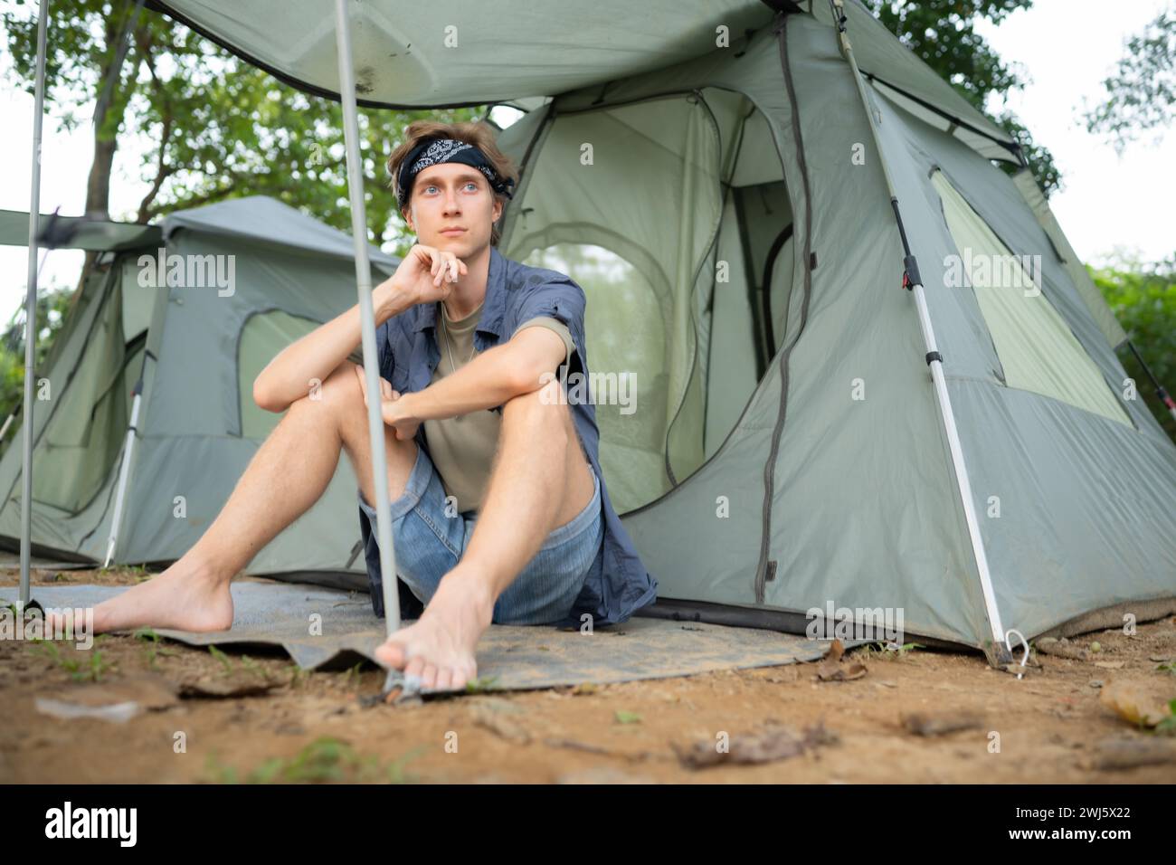 Giovane seduto di fronte alla tenda in campeggio in campagna Foto Stock