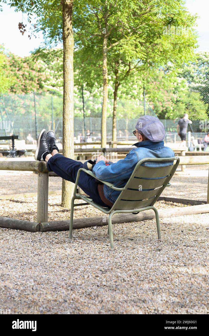 25.04. 2018 - Francia, Parigi - Una persona sdraia su una sedia del parco, godendosi una giornata di sole all'aperto, rilassandosi e divertendosi, bilanciando la vita lavorativa, sel Foto Stock