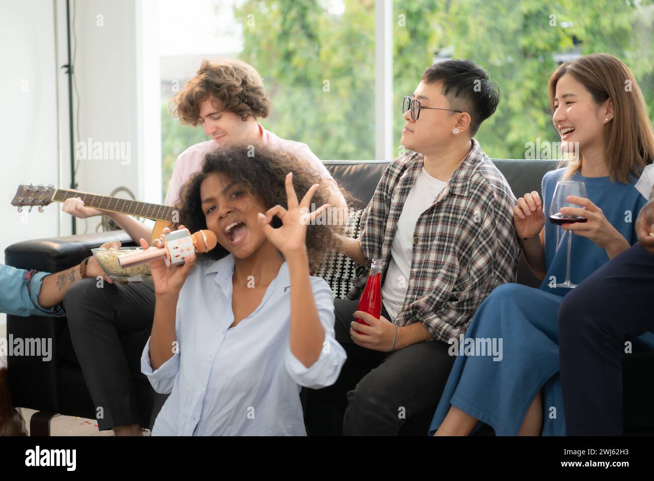 Gruppo di amici multietnici che si divertono alla festa suonando la chitarra e cantando insieme a casa. Foto Stock