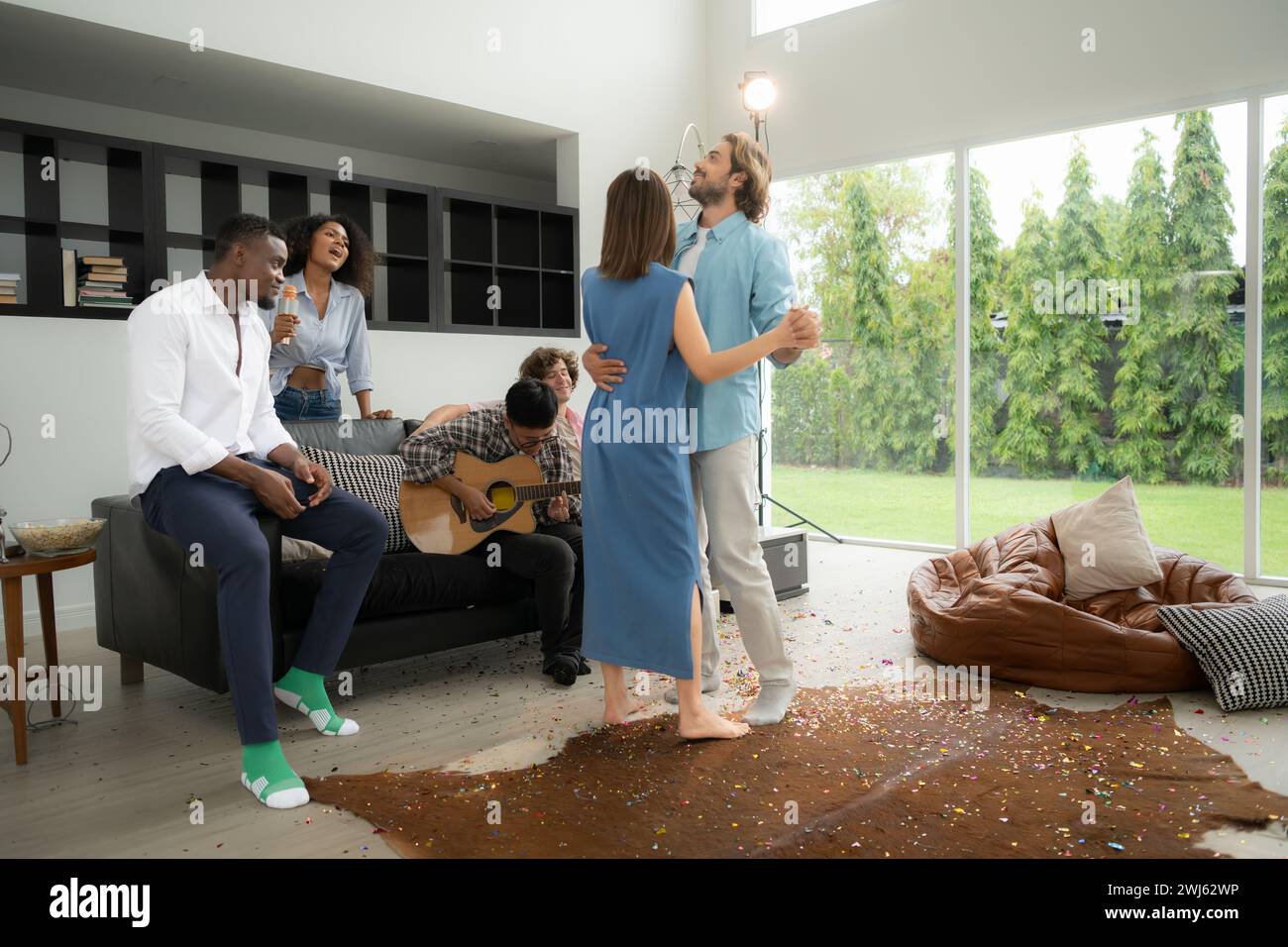 Gruppo di amici multietnici che si divertono alla festa suonando la chitarra, cantando e ballando insieme a casa. Foto Stock