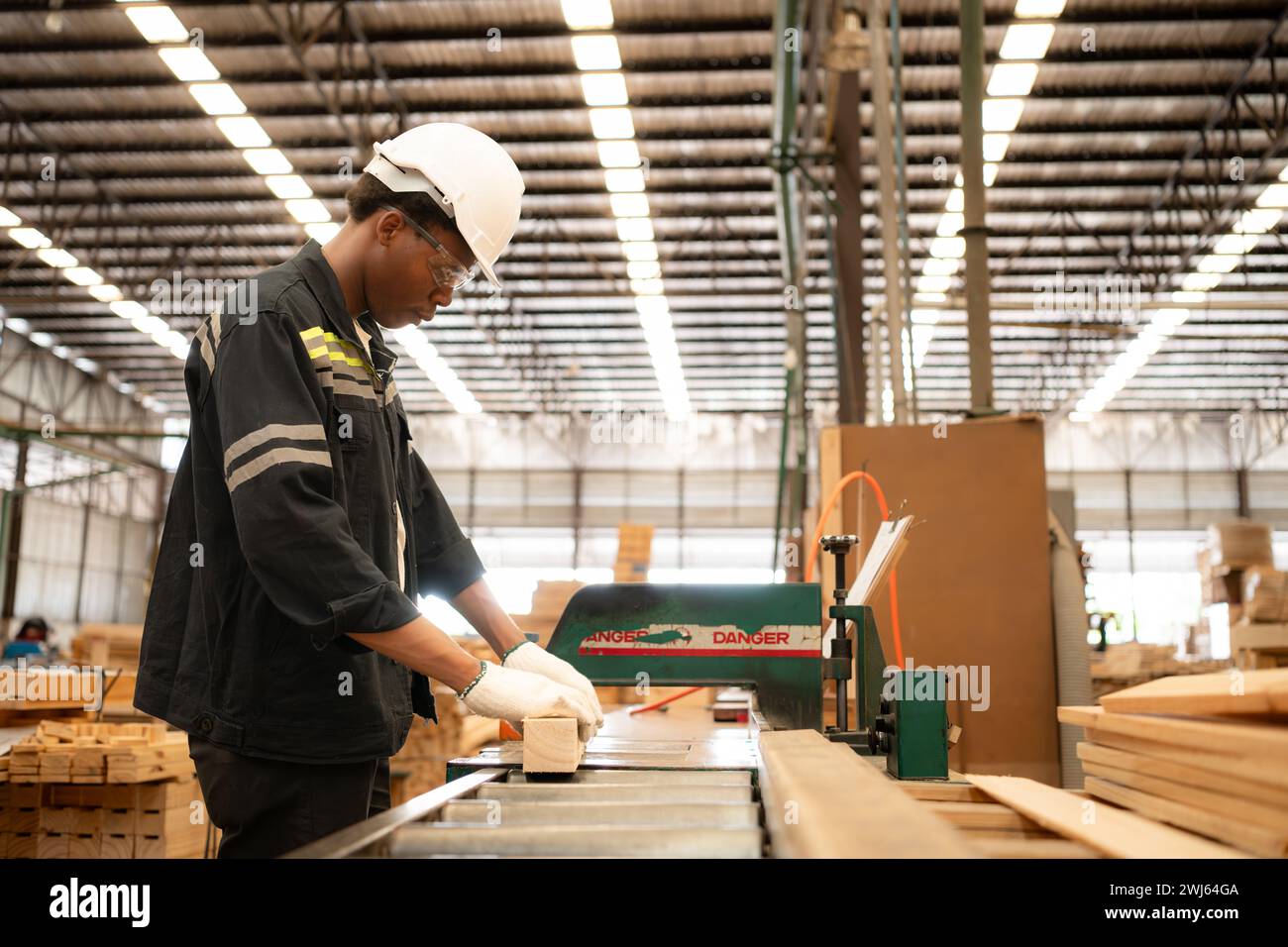 Un giovane lavoratore lavora in una fabbrica di lavorazione del legno, lavorando con macchine per segare e tagliare il legno per produrre lastre di legno per il makin Foto Stock