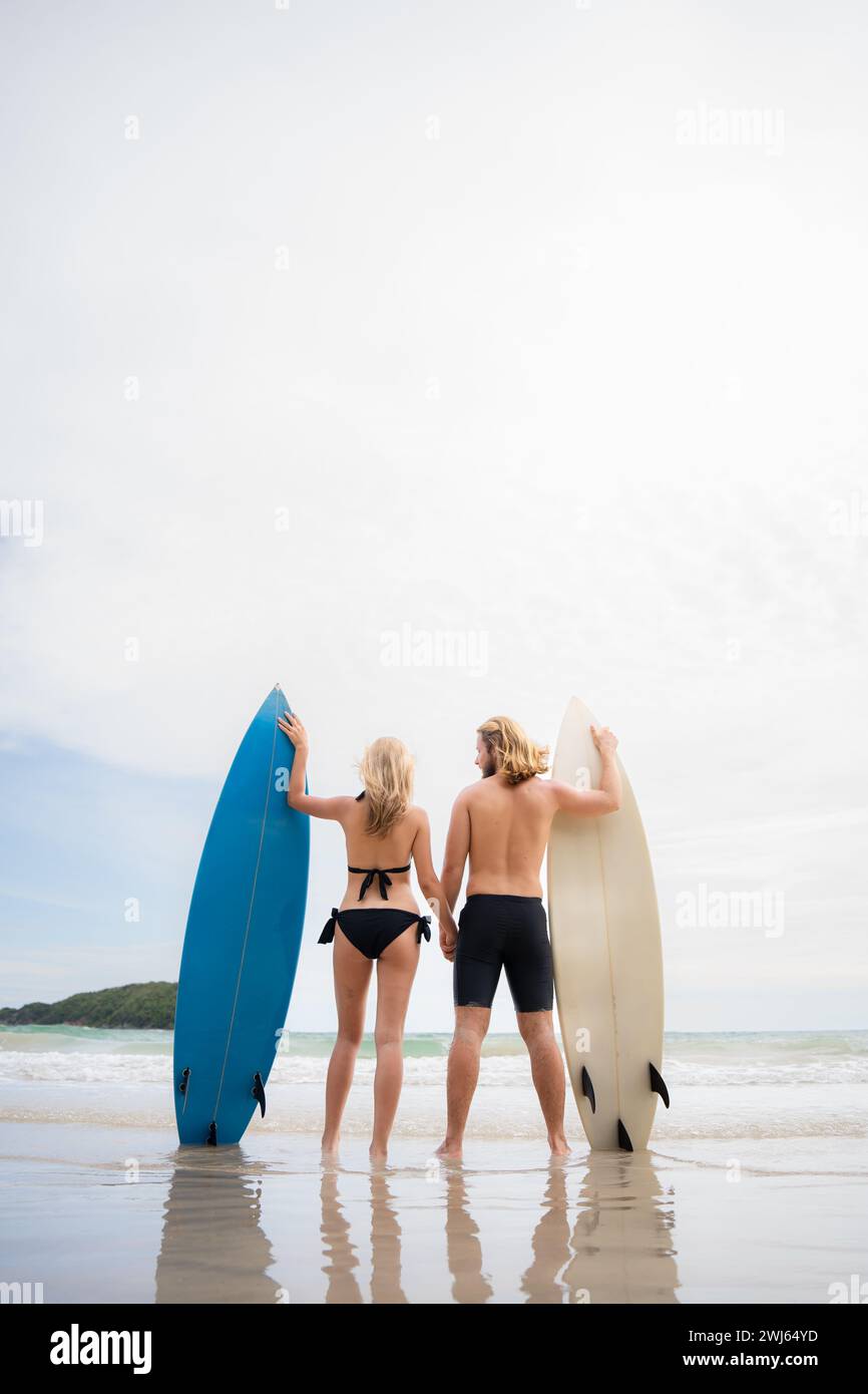 Vista posteriore del giovane uomo e della donna in costume da bagno con tavole da surf sulla spiaggia. Foto Stock