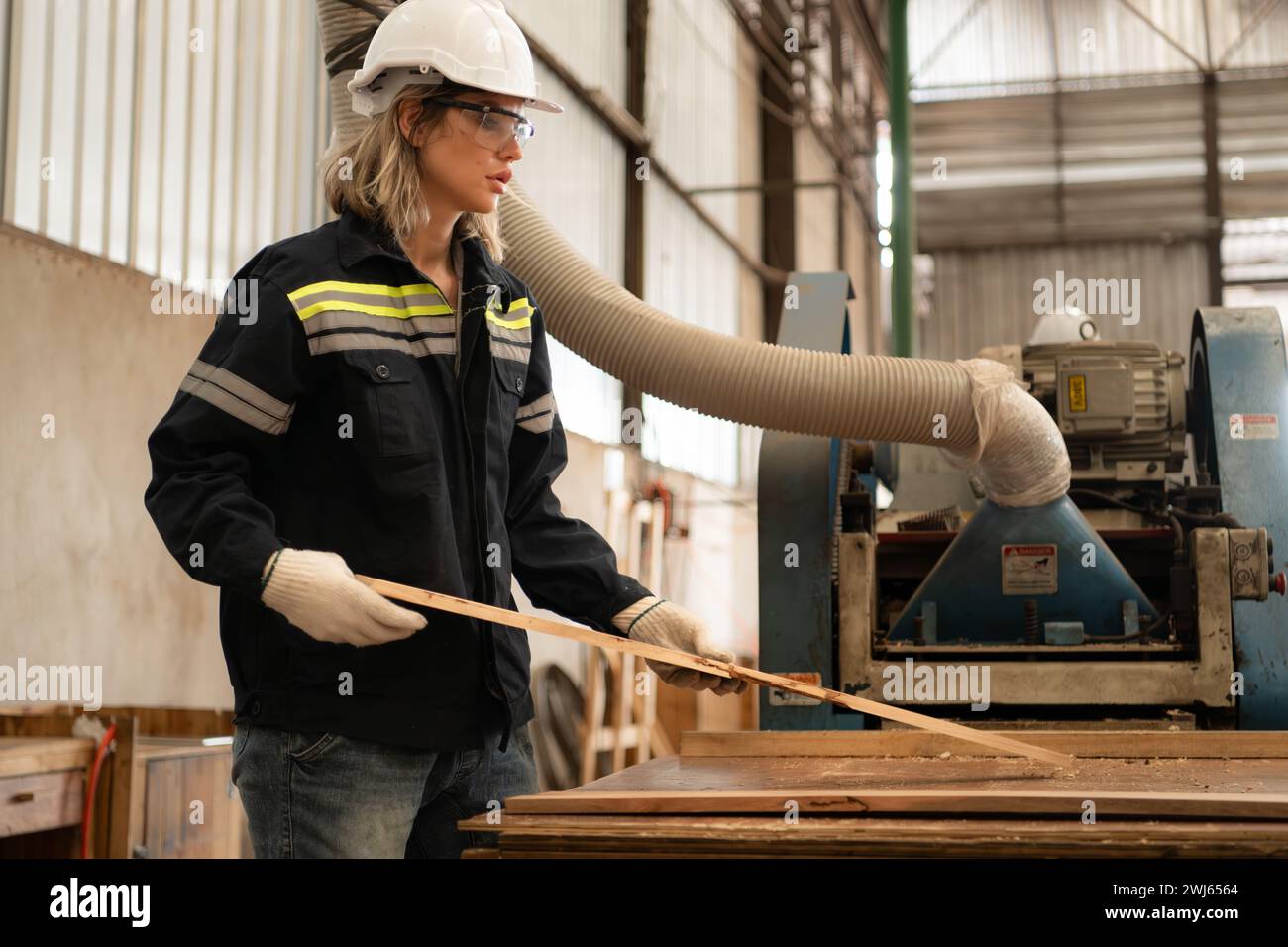 Un falegname lavora in un'officina di falegnameria. Raccoglie il legno che passa attraverso la smerigliatrice angolare per legno. Foto Stock