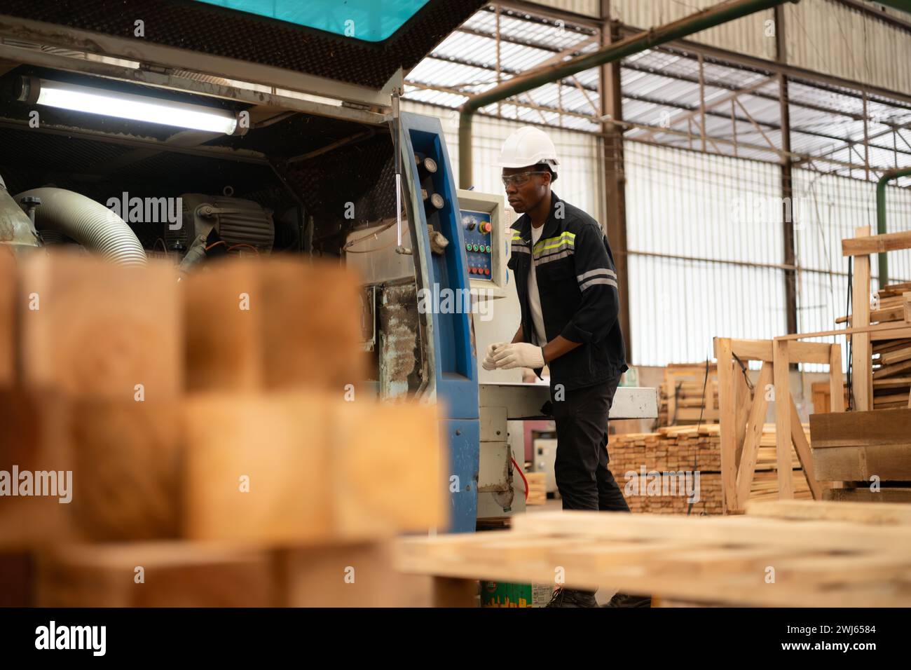 Un giovane lavoratore lavora in una fabbrica di lavorazione del legno, lavorando con macchine per segare e tagliare il legno per produrre lastre di legno per il makin Foto Stock