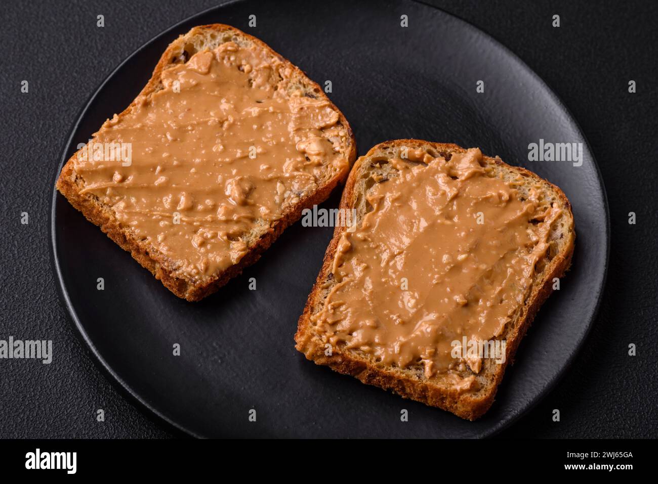 Sandwich nutriente composto da pane e burro di arachidi su un piatto di ceramica nera Foto Stock