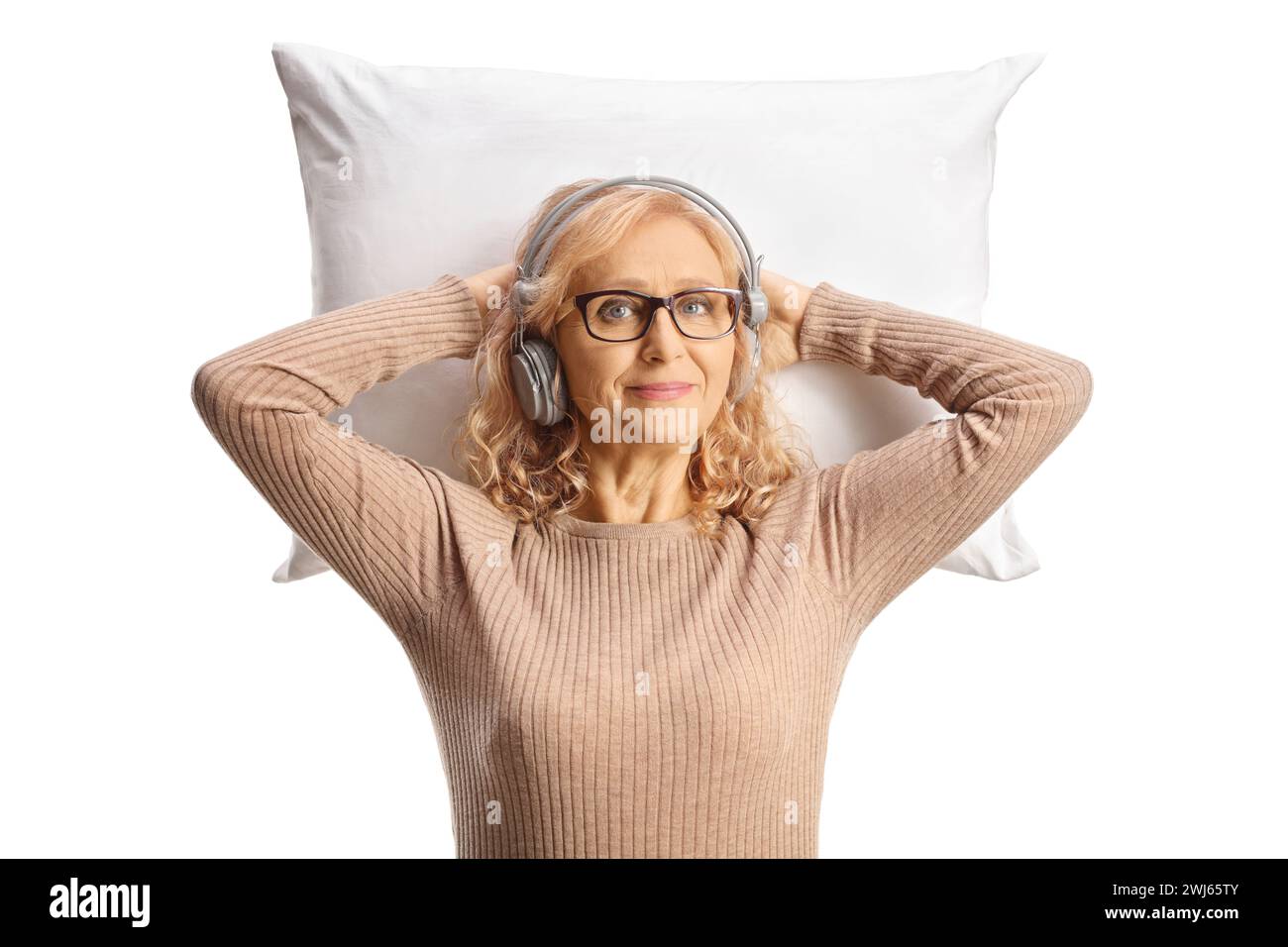 Donna di mezza età con cuffie appoggiate su un cuscino isolato su sfondo bianco Foto Stock