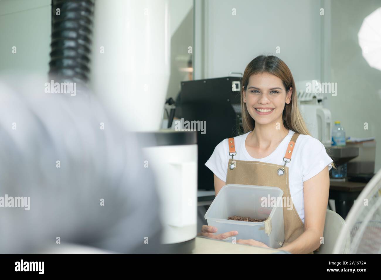 Giovane donna in grembiule che utilizza un tablet digitale per controllare la qualità dei chicchi di caffè con torrefazione digitale Foto Stock