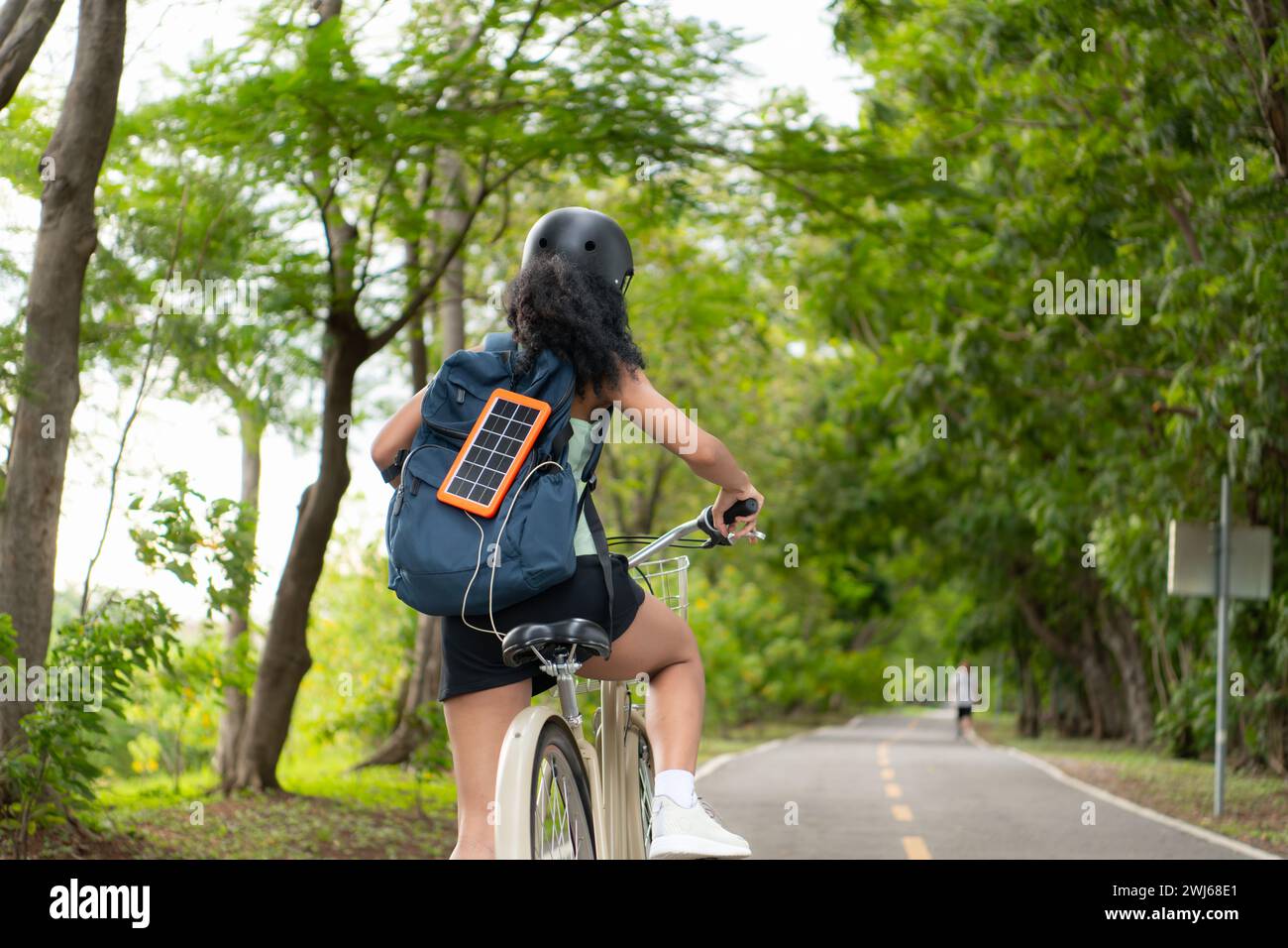 Vista posteriore di una donna asiatica in bicicletta nel parco. È dotato di uno zaino con pannello solare per ricaricare lo smartphone. Foto Stock