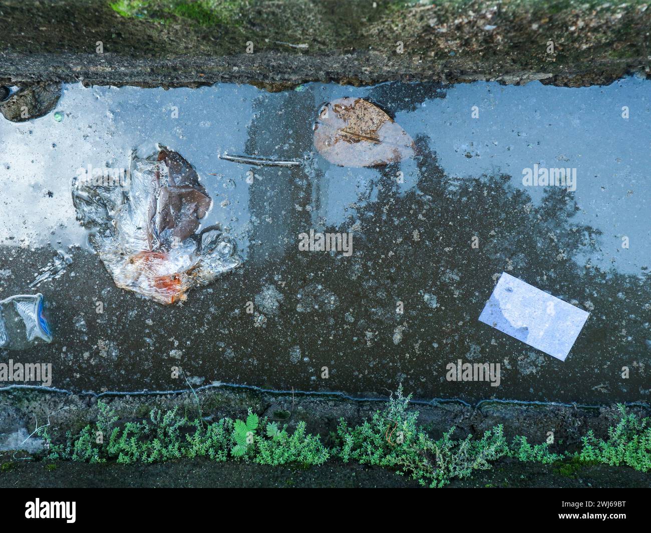 Le condizioni ambientali non sono pulite, si possono vedere rifiuti nelle grondaie d'acqua Foto Stock