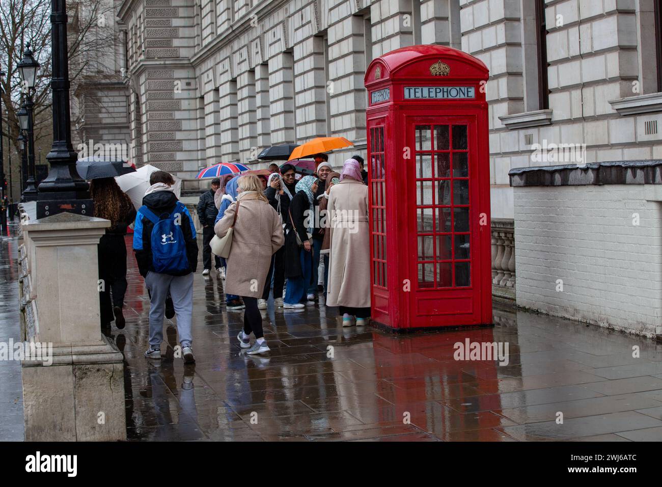 Londra, Regno Unito, 13 febbraio 2024 fila turistica sotto la pioggia con ombrelloni per scattare foto dell'iconica cabina telefonica rossa di Londra e godersi i siti di Londra nonostante la pioggia credito: Richard Lincoln/Alamy Live News Foto Stock
