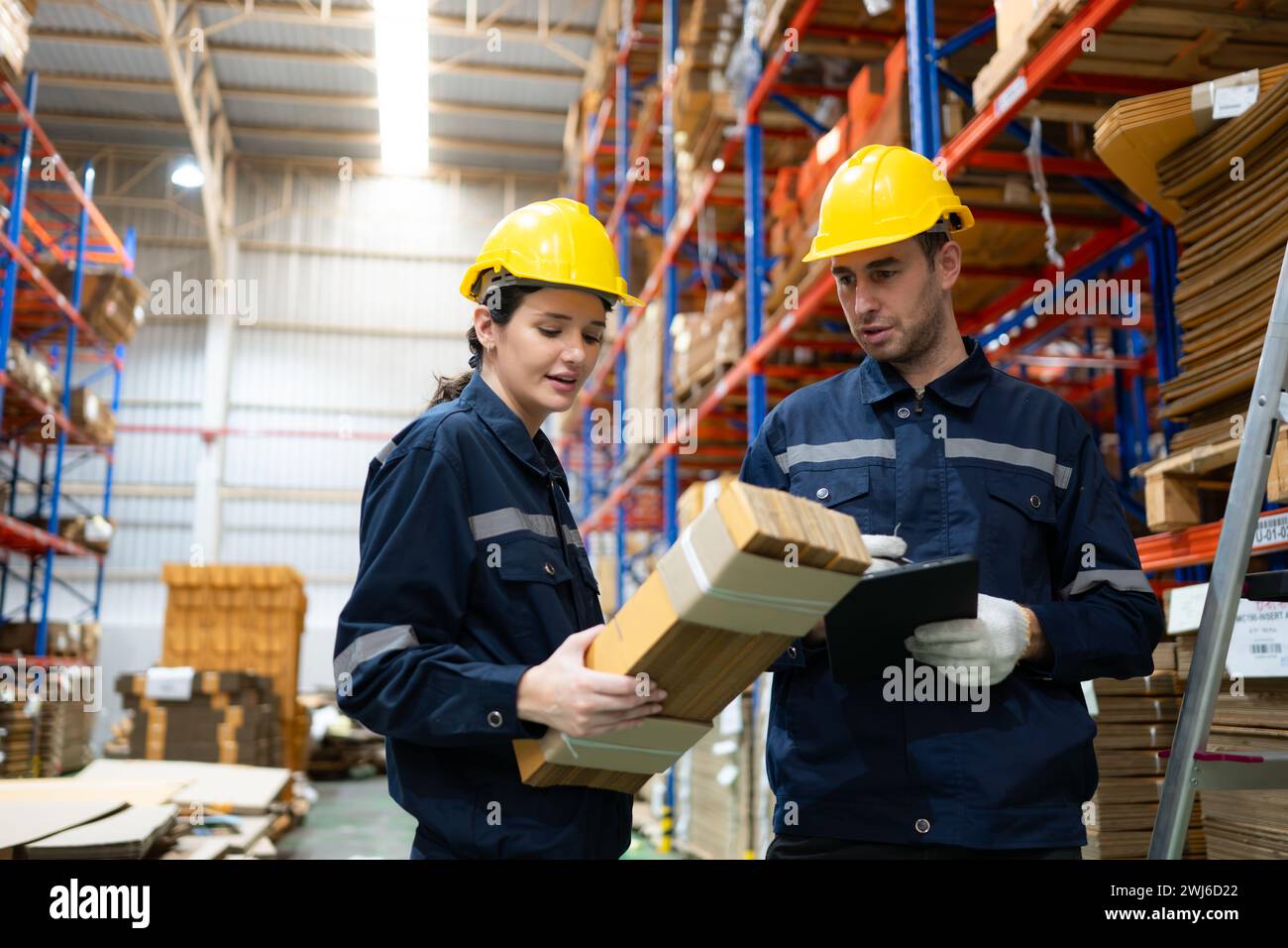 Una giovane lavoratrice di magazzino controlla e conta le scatole di cartone presenti nel magazzino utilizzando un tablet digitale. Foto Stock