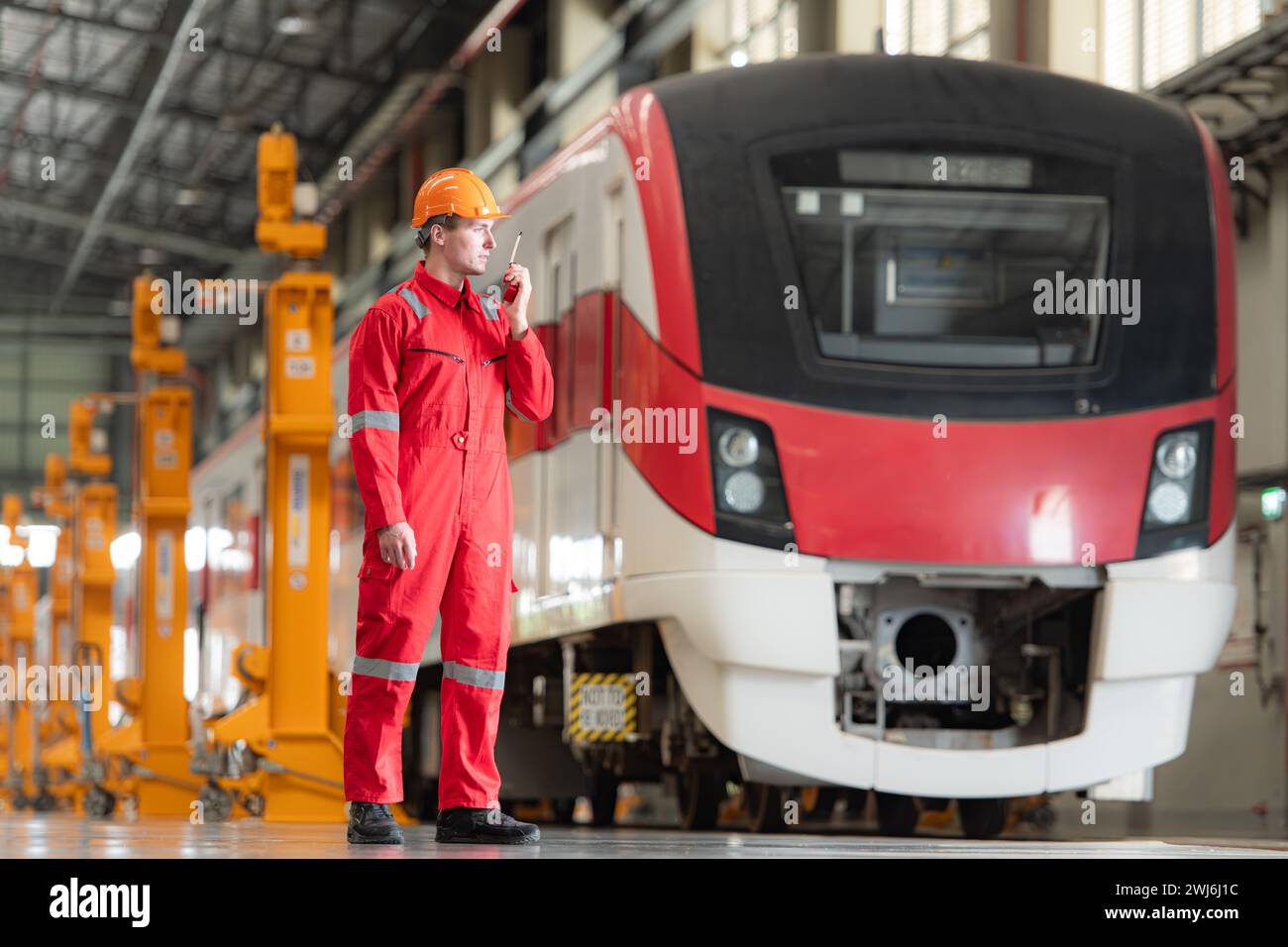 Ritratto di un tecnico che utilizza un walkie talkie di fronte a un treno per comunicare con i suoi colleghi dopo aver ispezionato l'impianto elettrico Foto Stock