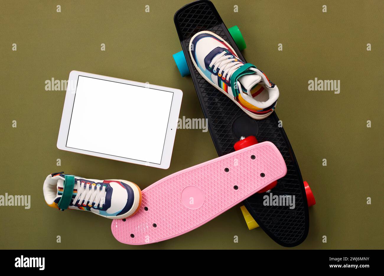Tablet moderno, skateboard e scarpe su sfondo verde oliva, piatto. Spazio per il testo Foto Stock