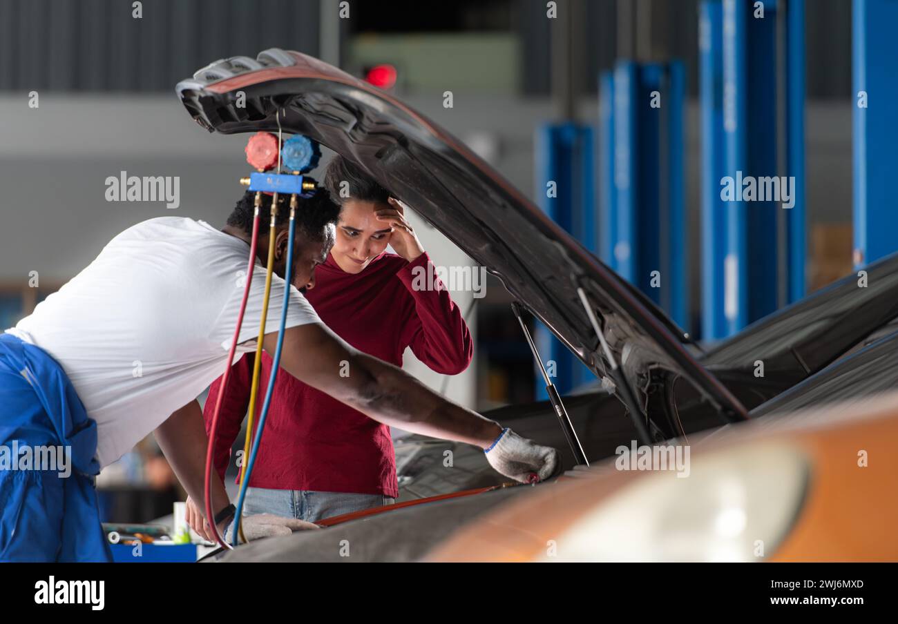 Il meccanico che lavora in un'officina di riparazione auto spiega al cliente dopo aver ispezionato il funzionamento del condizionatore d'aria e. Foto Stock