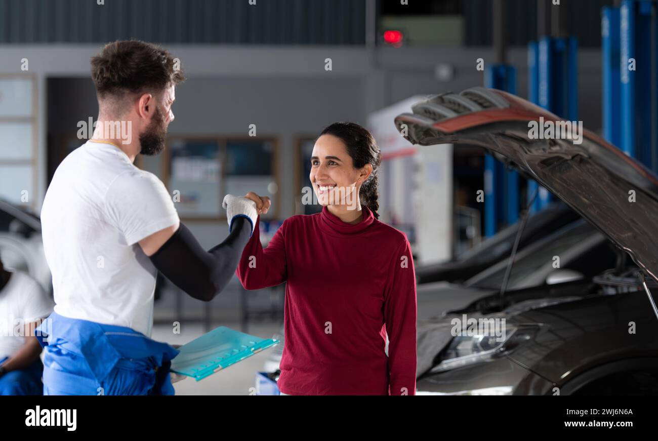 In un'officina di riparazione auto, Un meccanico professionista di auto informa una cliente donna sul costo delle riparazioni e riscuote la retribuzione Foto Stock