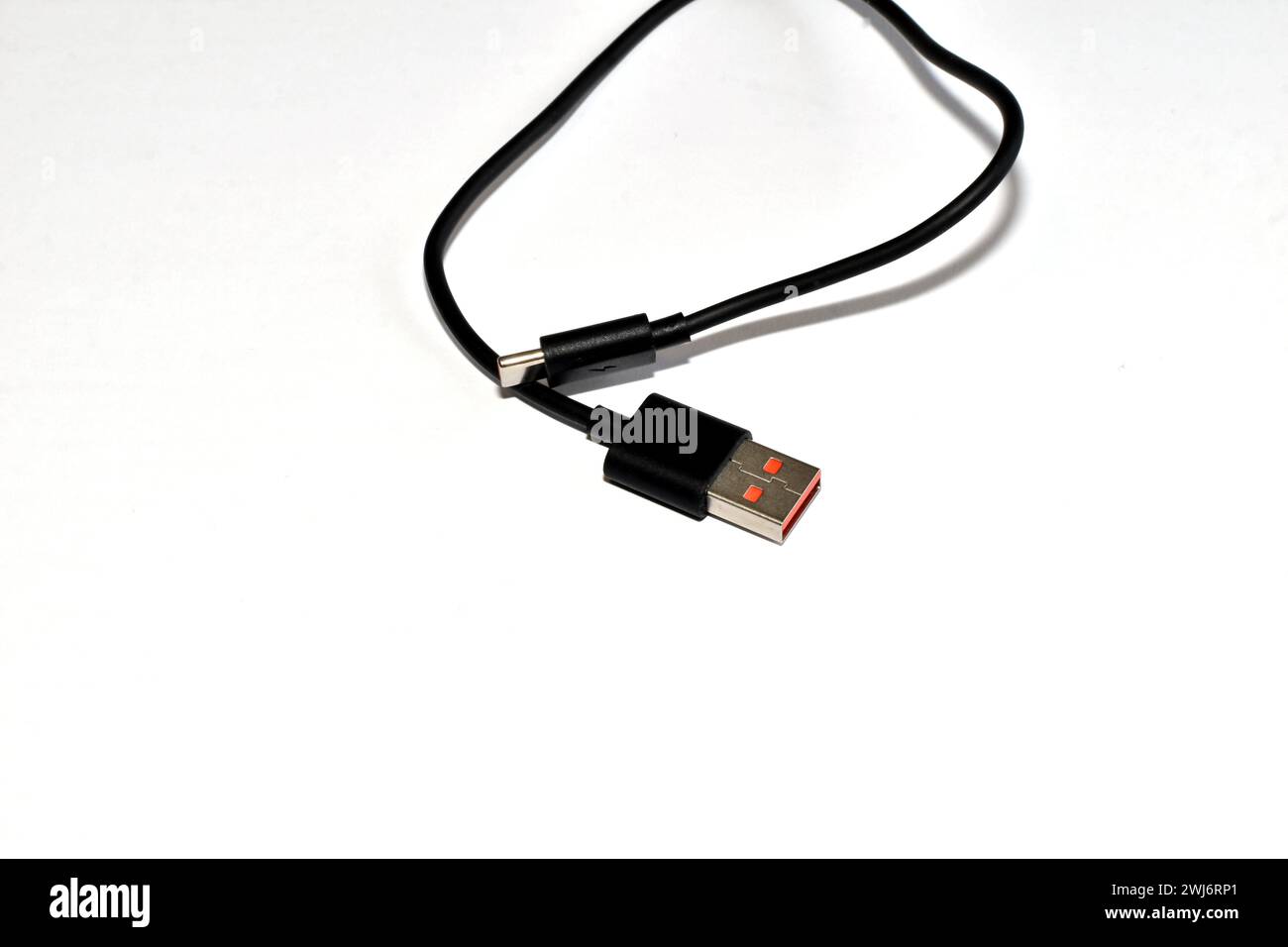 Un cavo USB corto di un corpo nero si trova in modo casuale su uno sfondo bianco. Foto Stock