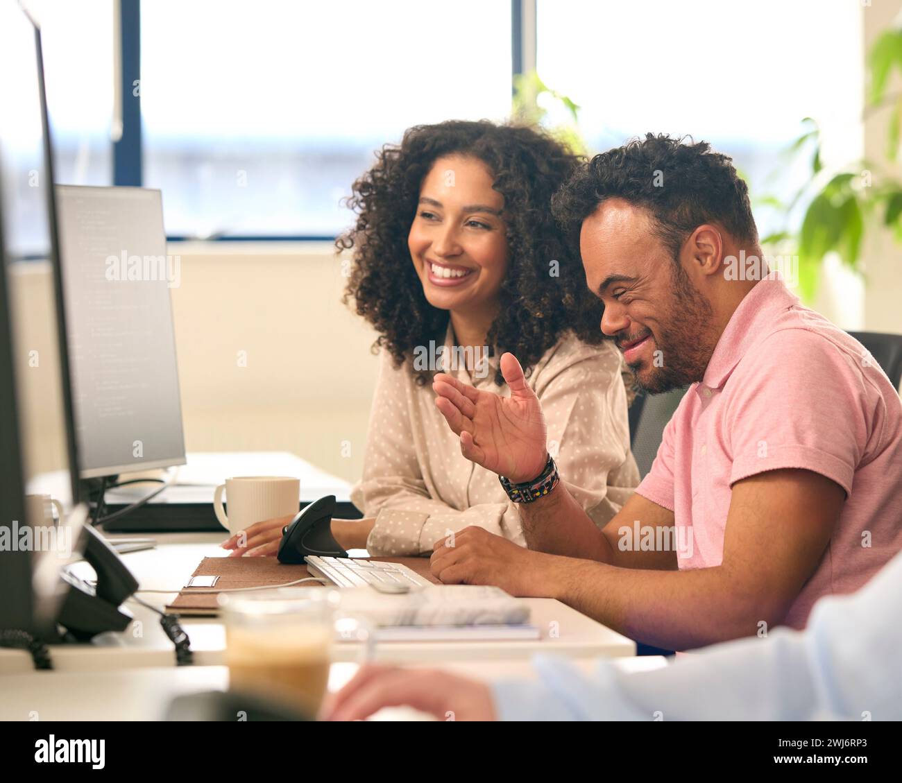 Donna che lavora in ufficio per la formazione professionale uomo con sindrome di Down che utilizza il computer Foto Stock
