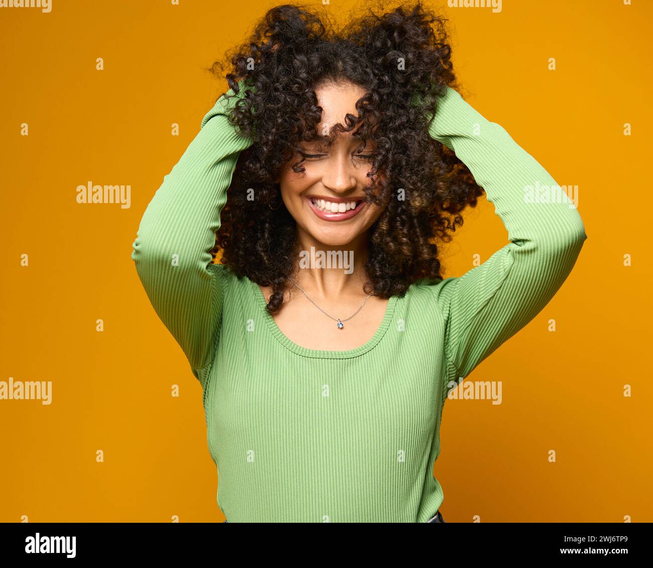 Studio Ritratto di donna sorridente in piedi su sfondo giallo che regge i capelli Foto Stock