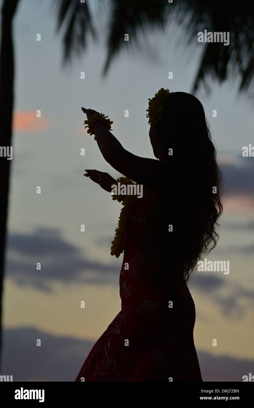 Una giovane ballerina hula si esibisce sulla riva di Waikiki Beach alle Hawaii, mentre il cielo del tramonto la rende in silhouette Foto Stock