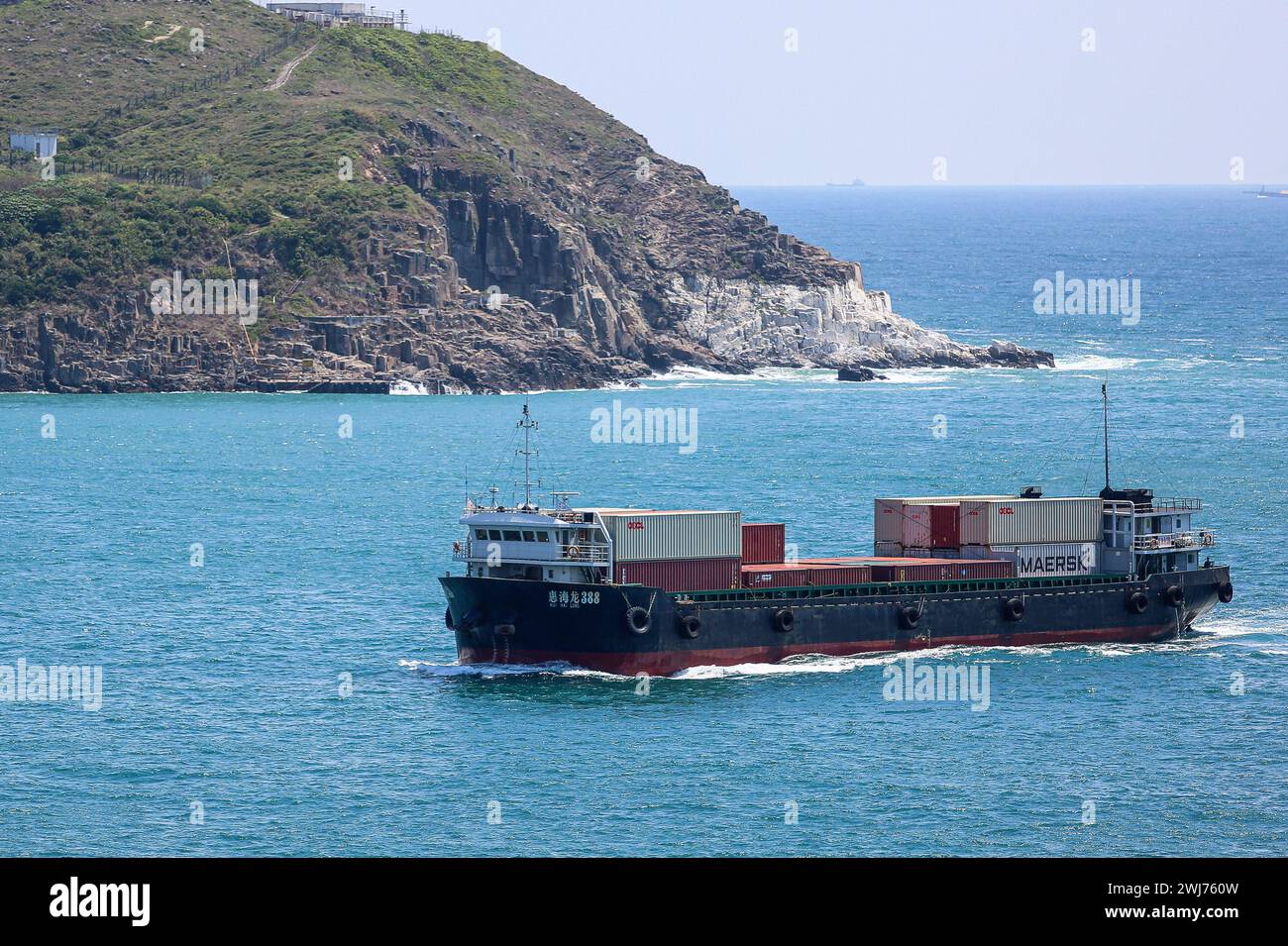 Piccola nave da carico per container HUI hai LONG 388 caricata con container che entrano nel canale di Tathong a Hong-Kong, scogliere rocciose e grotte dell'isola di Tung Lung Chau Foto Stock