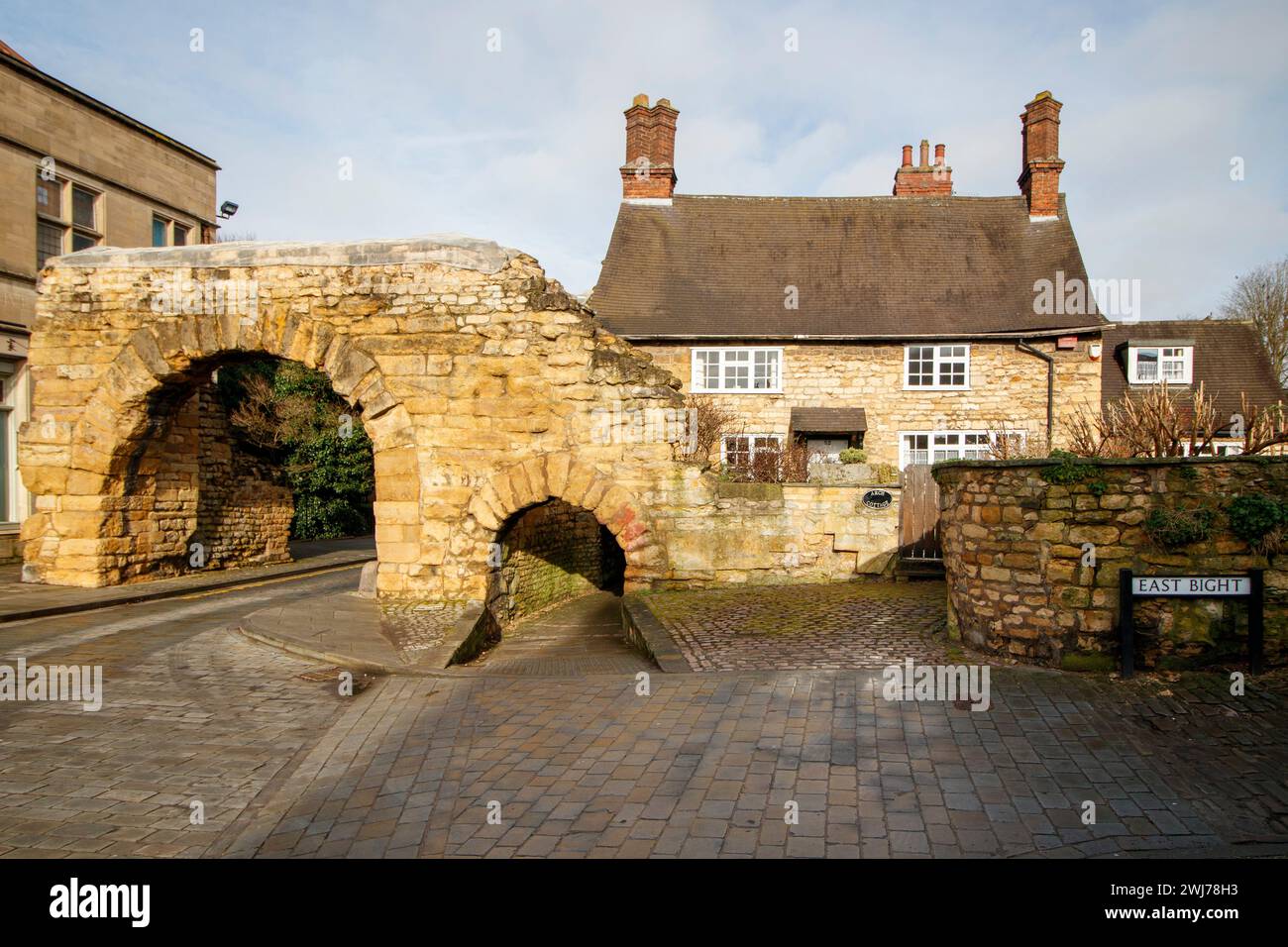 Il Newport Arch e la strada che porta a Bailgate, l'area superiore di Lincoln. Newport Arch è una porta romana del III secolo nella città di Lincoln, nel Lincolnshire. Si tratta di un monumento e di un edificio classificato di grado i ed è considerato l'arco più antico del Regno Unito ancora utilizzato dal traffico. Foto Stock