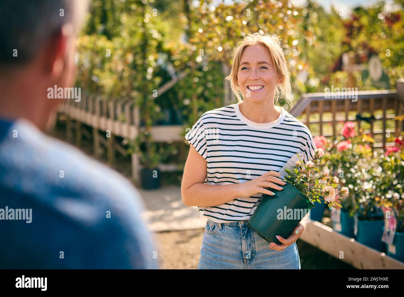 Donna all'aperto nel Garden Centre che chiede consigli all'assistente vendite che sceglie e acquista Rose Foto Stock