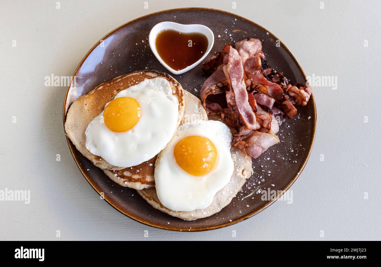 Deliziosa colazione fatta in casa con pancetta croccante, uova e frittelle dolci Foto Stock