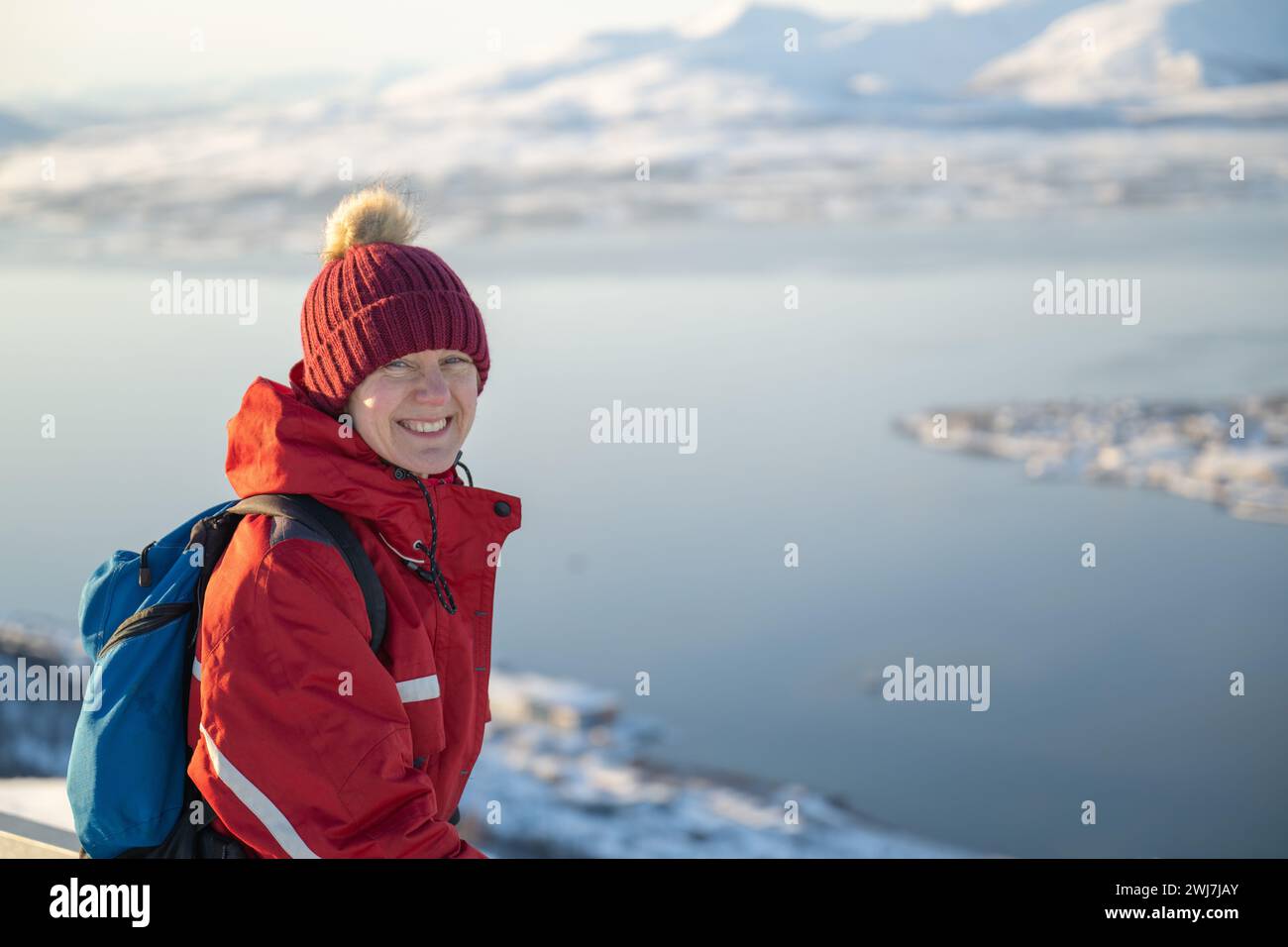 Donna bianca vestita con equipaggiamento invernale in cima alla funivia da Tromsø, ammirando il panorama in una giornata luminosa, soleggiata e invernale. Foto Stock