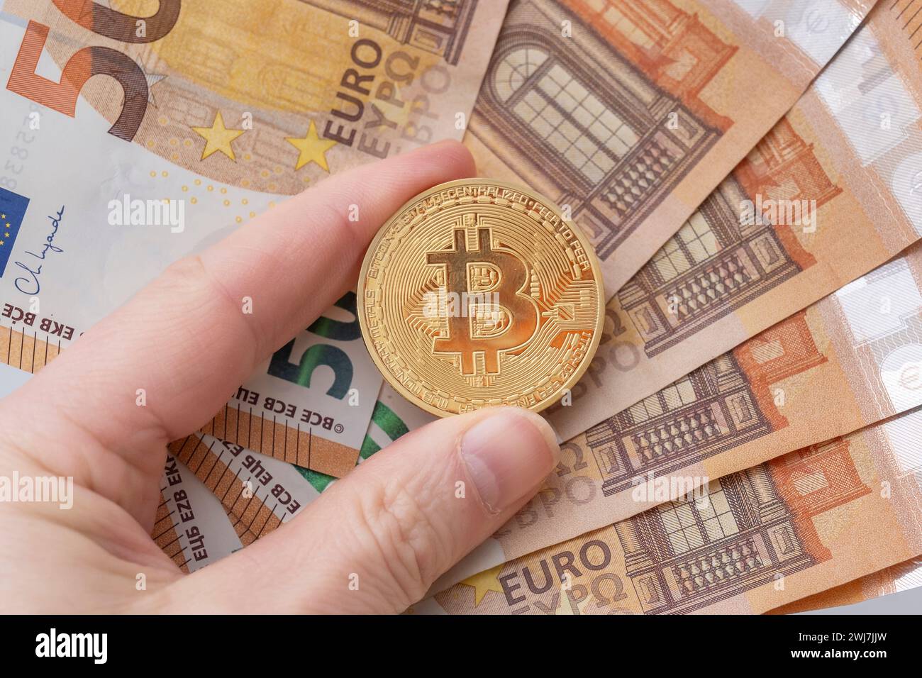 Moneta Bitcoin tra le dita rispetto alle banconote in euro Foto Stock
