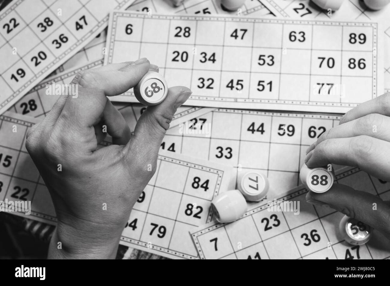 Giocare a lotto, bianco e nero. Persona che tiene un cubo con il personaggio sullo sfondo della scheda bingo, monocromatica. Stile di vita nostalgico. Giochi da tavolo. Foto Stock