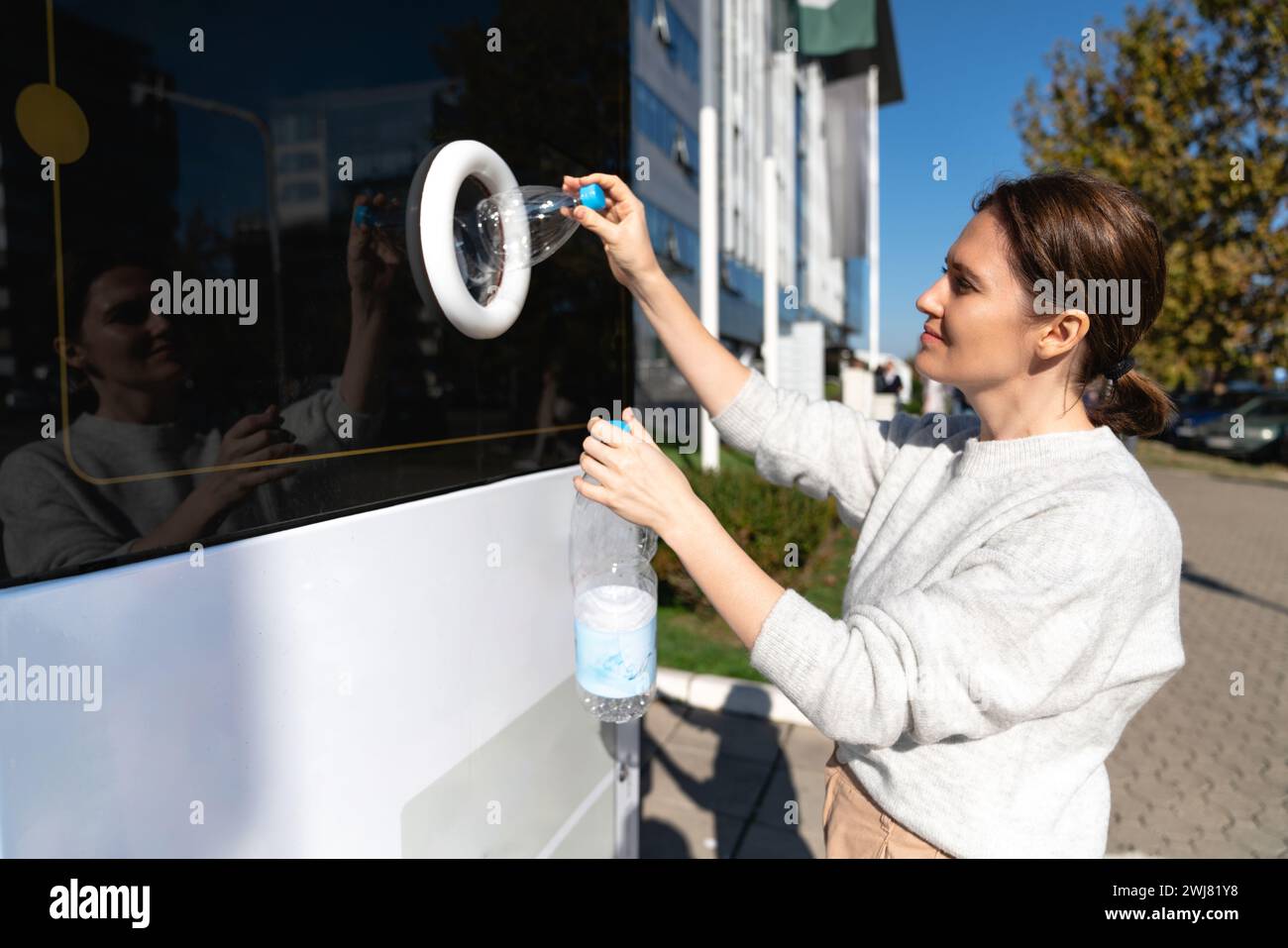 La donna usa una macchina self-service per ricevere bottiglie e lattine di plastica usate in una strada cittadina. Foto Stock