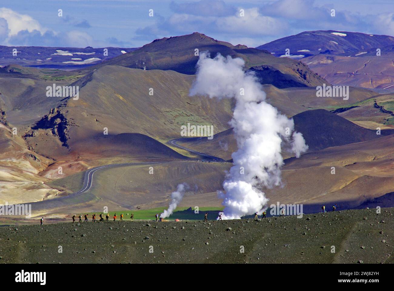 Gli escursionisti camminano attraverso paesaggi aridi e vulcanici su cui grumi di vapore derivanti dalla deriva dell'attività geotermica, Namafjall, Myvatn, Islanda Foto Stock