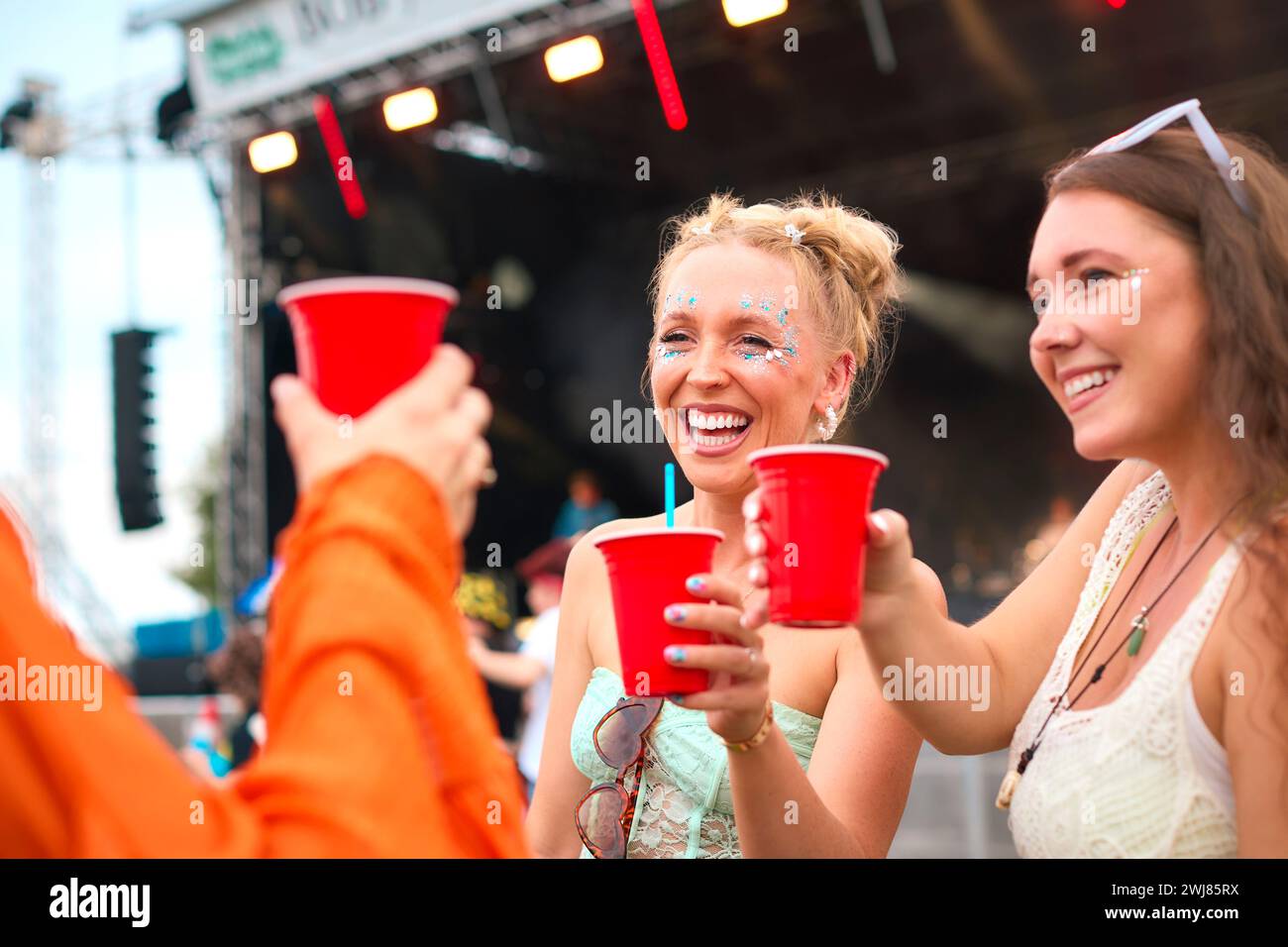 Tre amiche che indossano Glitter Having Fun al Summer Music Festival che tengono un drink Foto Stock