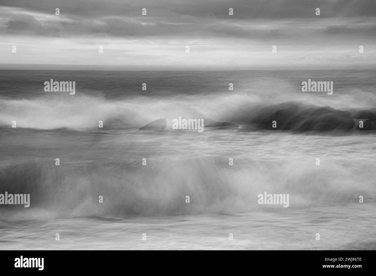 Otturatore lento e movimento intenzionale della fotocamera foto monocromatica di onde e rocce infranti sulla costa della Cornovaglia al Lizard di Dollar Cove, Gunwalloe Foto Stock