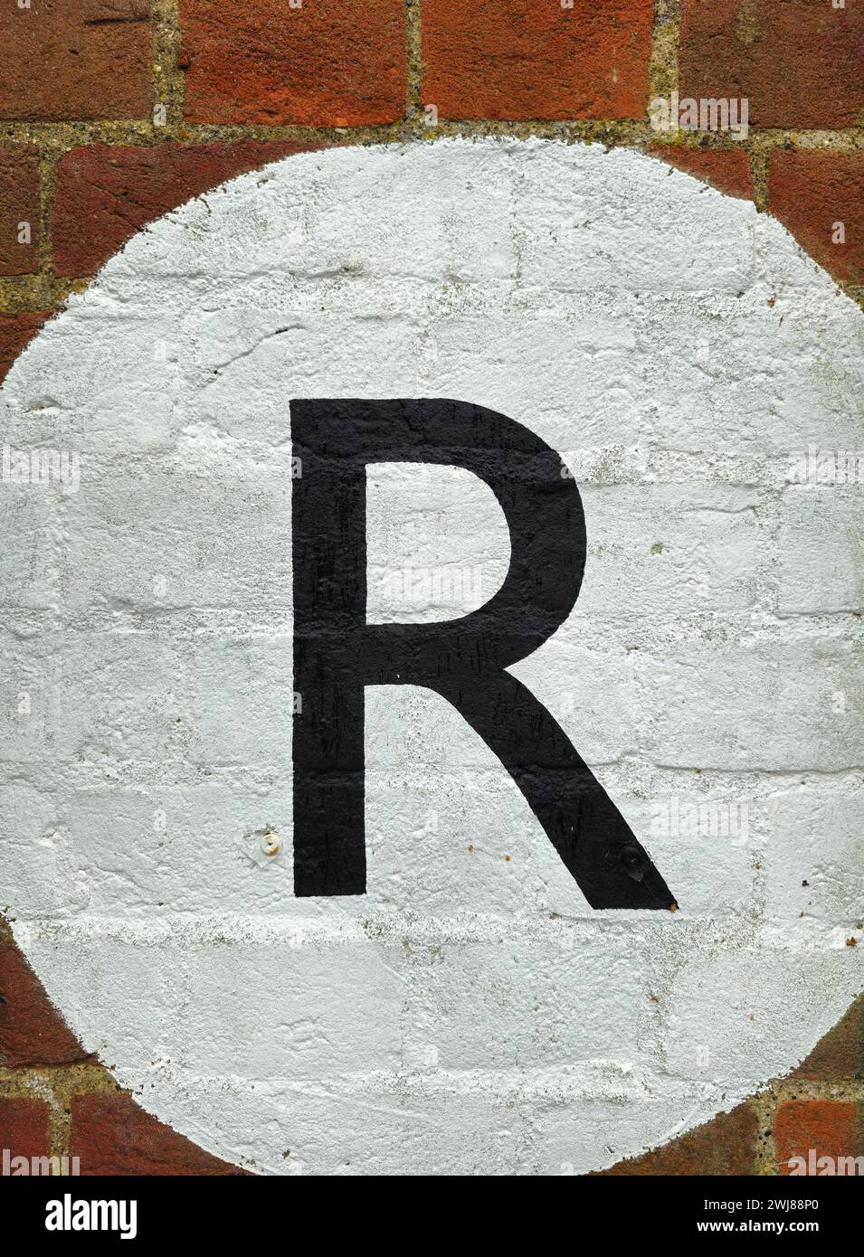 Lettera R in nero dipinta su un cerchio bianco su una parete di mattoni Foto Stock