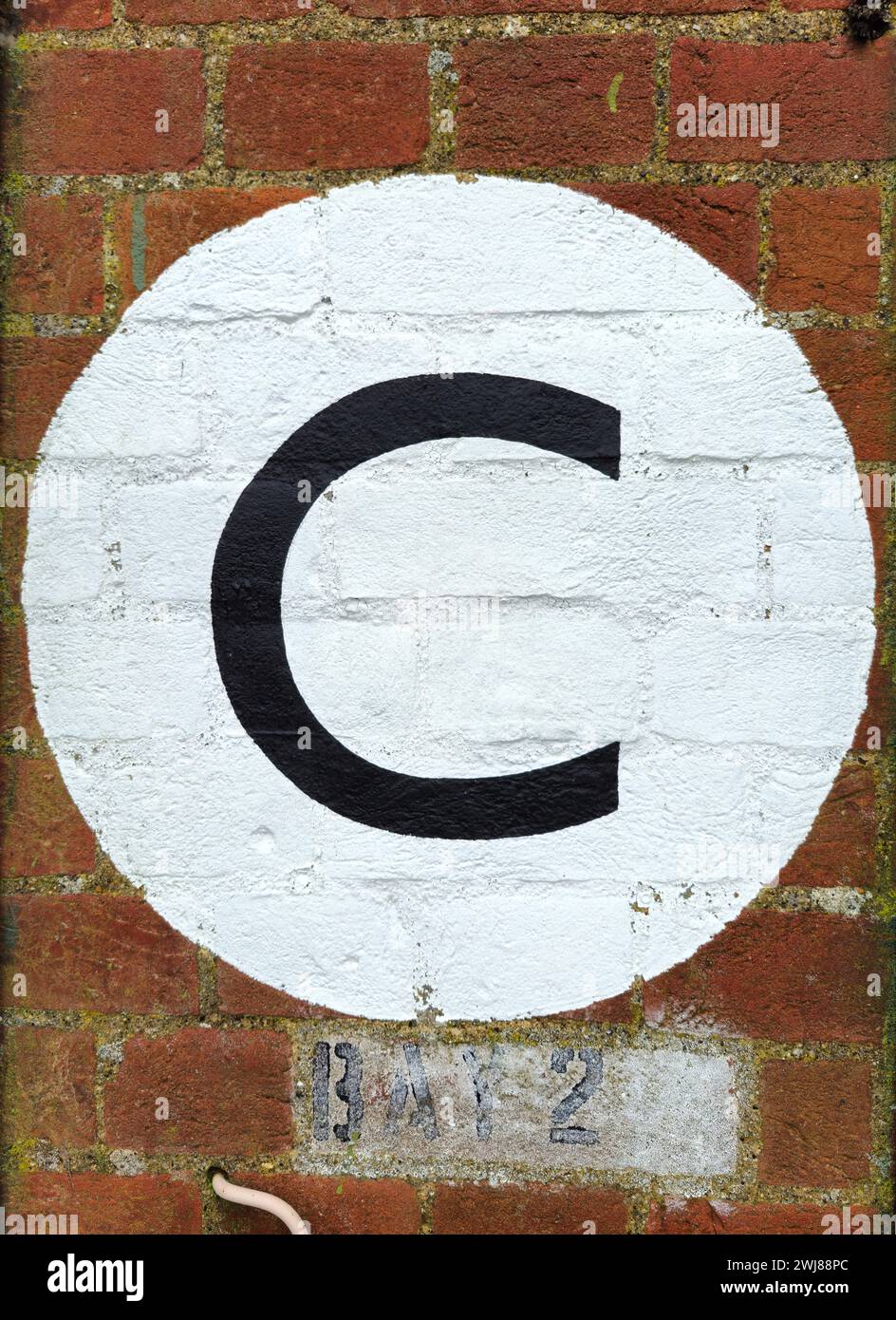 Lettera C in nero dipinta su un cerchio bianco su un muro di mattoni Foto Stock