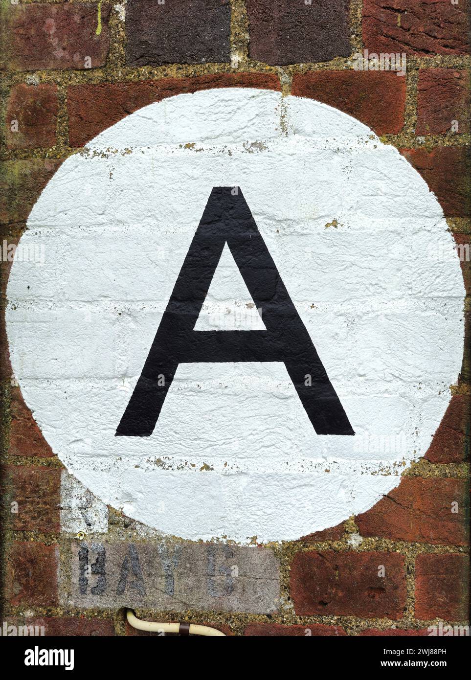 Lettera A in nero dipinta su un cerchio bianco su un muro di mattoni Foto Stock
