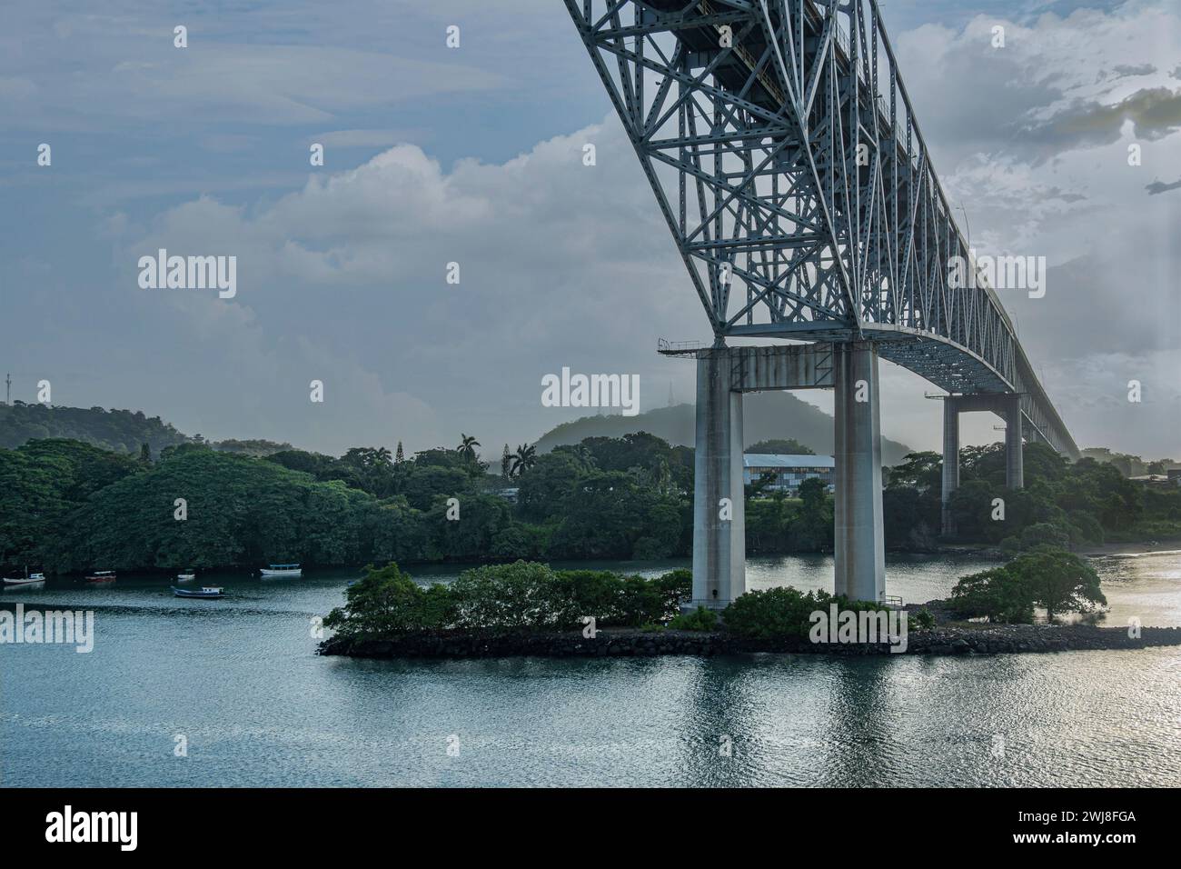 Canale di Panama, Panama - 24 luglio 2023: Navigazione sotto ponte sospeso delle Americhe. Paesaggio nuvoloso blu mattutino e cintura di alberi verdi sul litorale Foto Stock